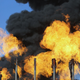 Gas flares at the Havana oil field in Iraq burn in front of black smoke.